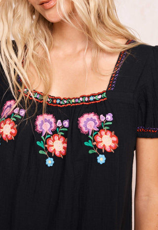 a-close-up-of-a-black-short-sleeve-bohemian-style-dress-featuring-colorful-floral-embroidery-on-the-chest-and-neckline-worn-by-a-model