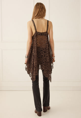 A woman shown from the back wearing a dark brown lace camisole top with thin straps, black pants, and brown shoes, standing against a white paneled wall.